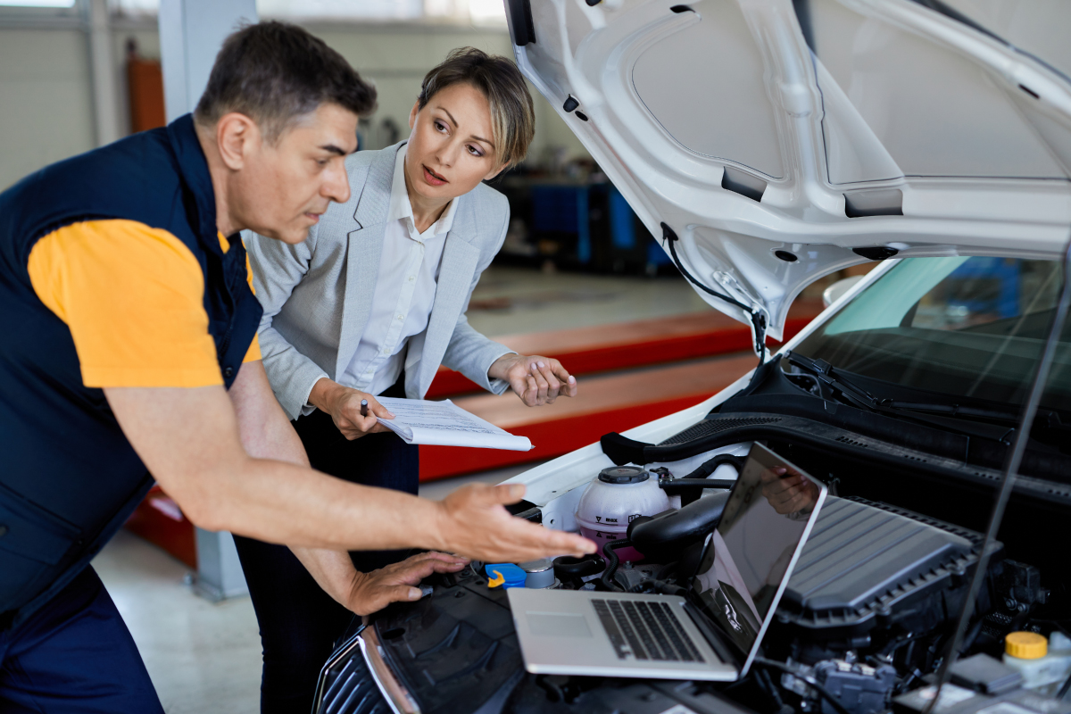 A lady manager and hybrid vehicle mechanic expertly looking at a laptop in the car workshop