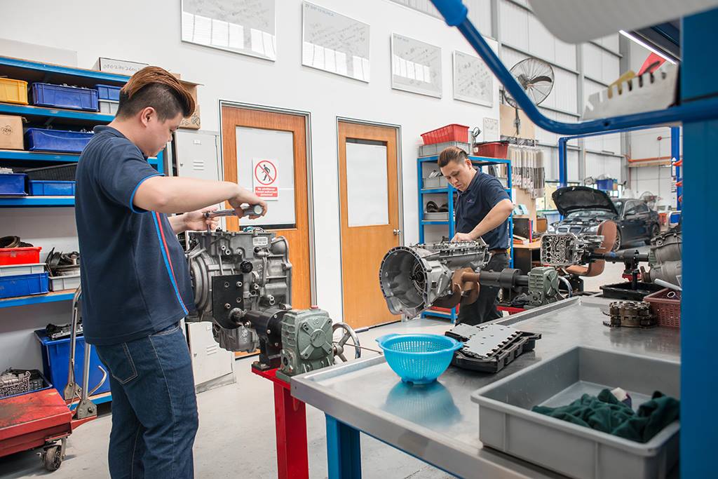 Two Hybrid Car Specialists inspecting a hybrid engine in a workshop.