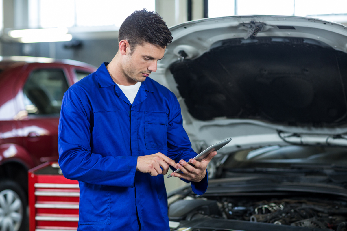 A Jackson Powertrain Hybrid Car Specialist mechanic using a tablet to diagnose issues in the automotive repair centre.