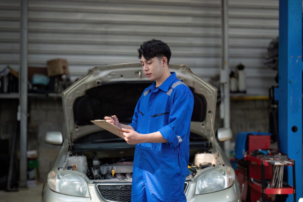 A Hybrid Car Specialist mechanic standing in front of a car with a clipboard.